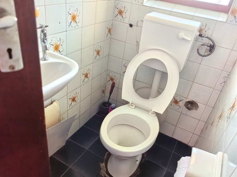 A small bathroom featuring a standard toilet and wall-mounted basin, currently requiring repairs to the flooring and wall tiling.