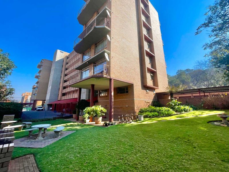 Exterior view of the apartment building featuring a well-maintained garden, paved patio area, and private balconies.
