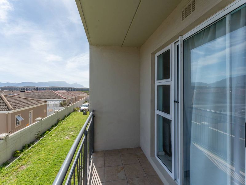 A covered balcony featuring tiled flooring, a metal balustrade, and sliding glass door access, offering views over the surrounding residential area.