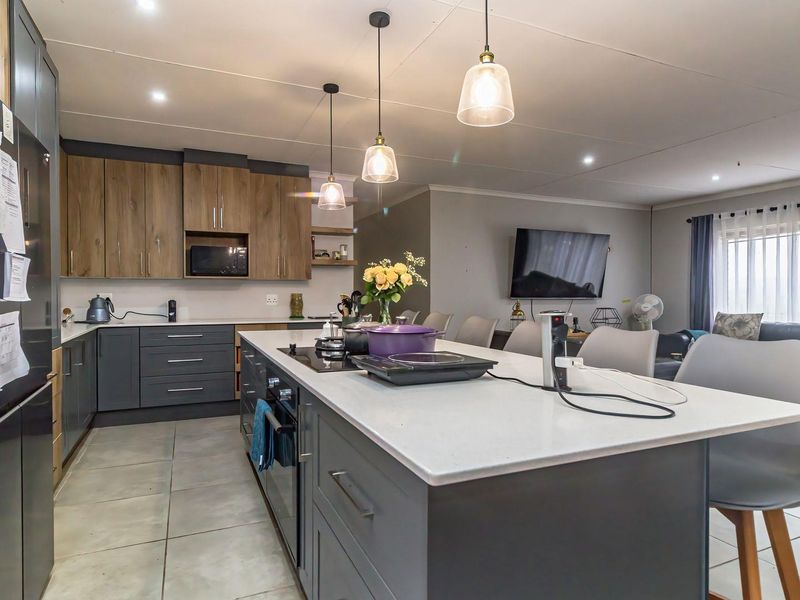 Modern open-plan kitchen and living area featuring a central island with quartz countertops, sleek cabinetry, and contemporary pendant lighting.