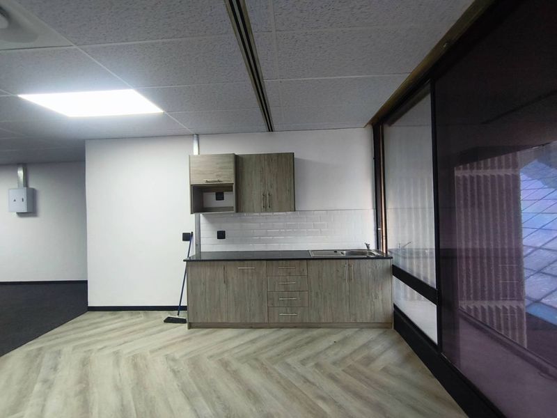 A modern office kitchenette featuring wood-grain cabinetry, a stainless steel sink, subway tile backsplash, and durable herringbone vinyl flooring.