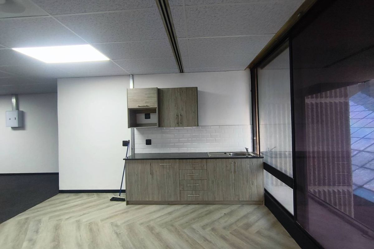 A modern office kitchenette featuring wood-grain cabinetry, a stainless steel sink, subway tile backsplash, and durable herringbone vinyl flooring.