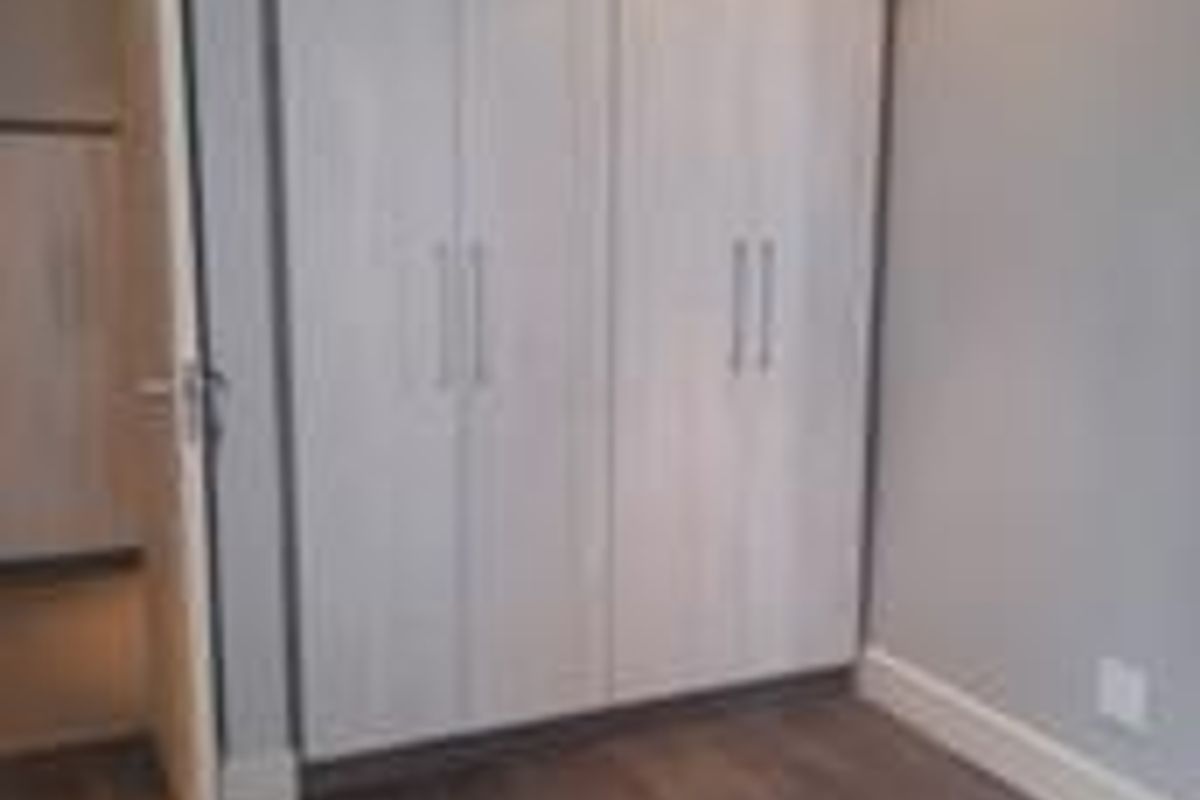 A bedroom featuring modern built-in cupboards with light wood-grain finish and dark trim, complemented by dark laminate flooring and recessed ceiling lighting.
