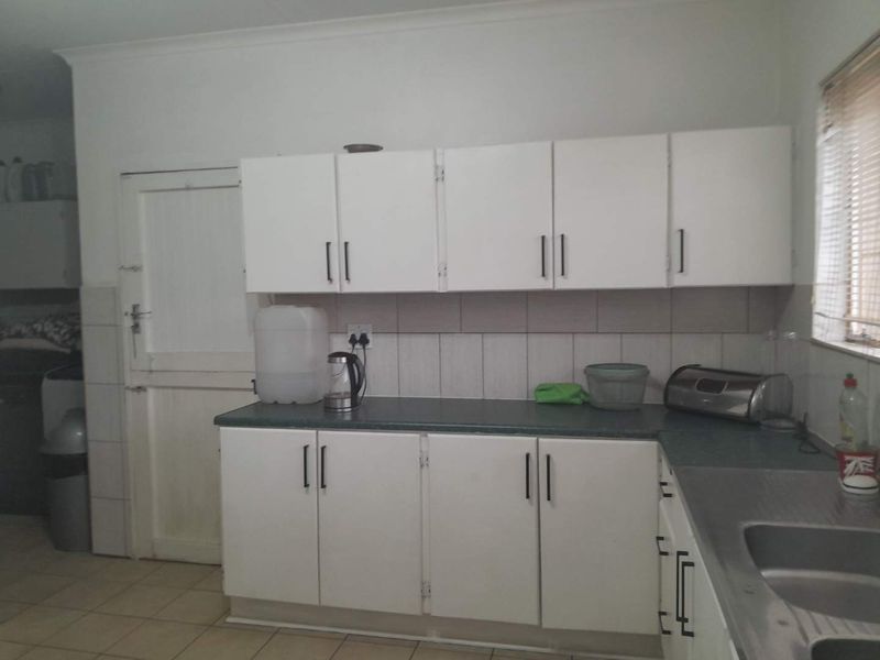 A functional kitchen featuring white built-in cabinetry, laminate countertops, a stainless steel sink, and tiled flooring, offering a practical layout for daily use.