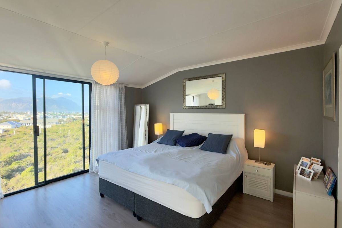 A bright bedroom featuring laminate flooring, a large sliding glass door with scenic views, and neutral grey wall finishes.