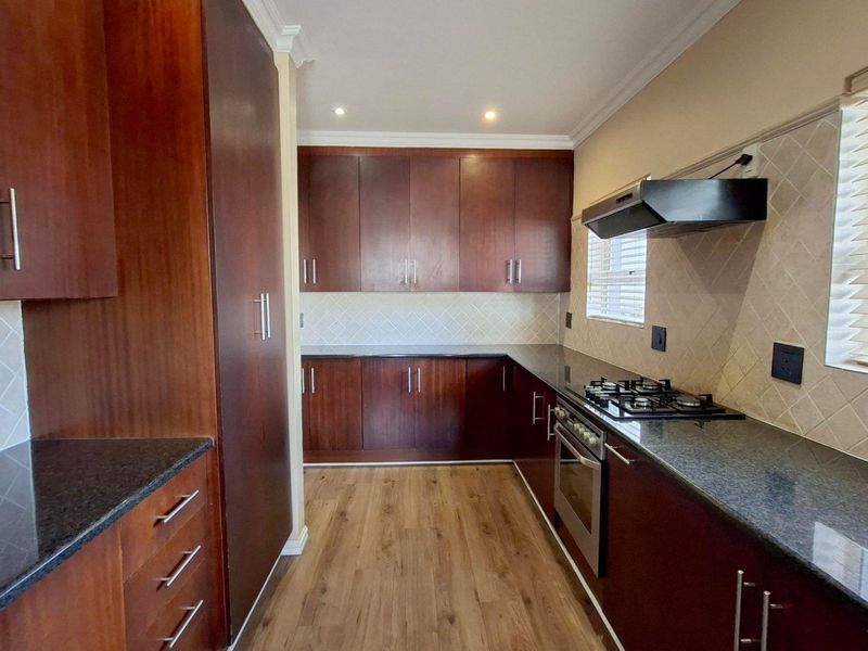 A well-maintained kitchen featuring dark wood cabinetry, granite countertops, a gas hob, built-in oven, and modern laminate flooring.