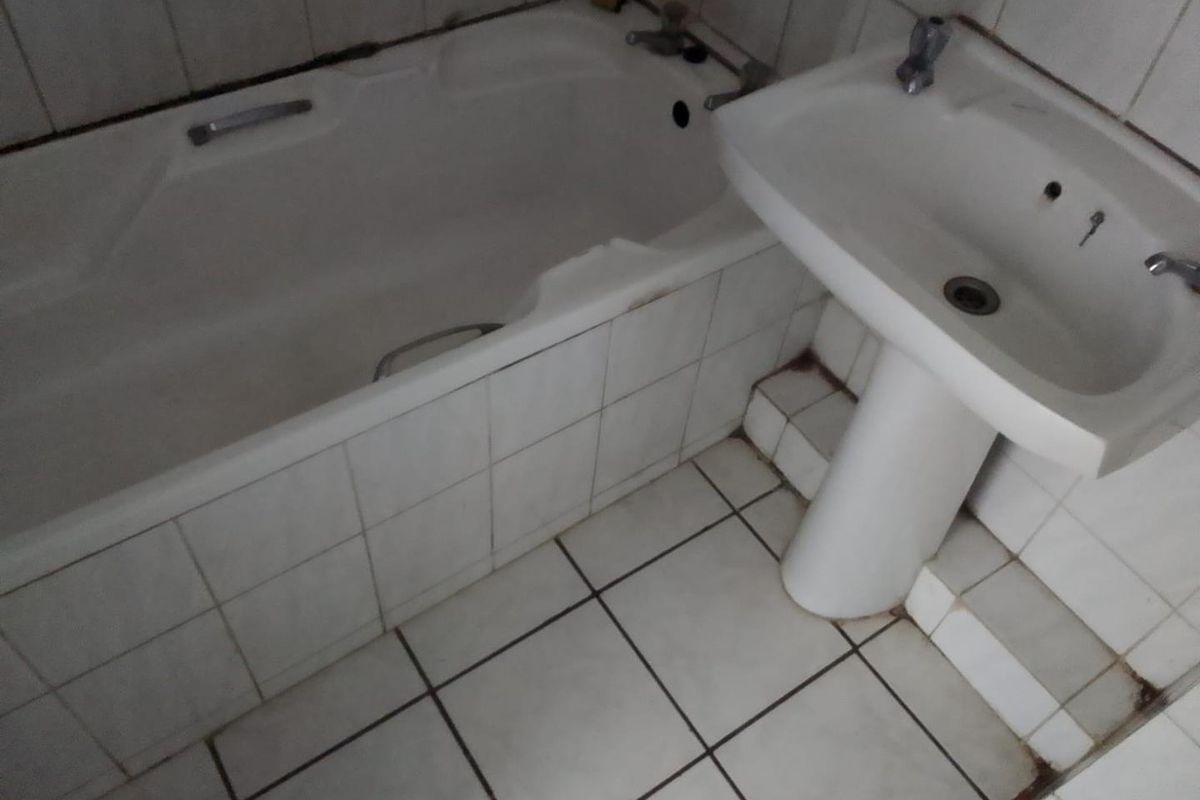 A functional bathroom featuring a standard bathtub and pedestal basin with tiled finishes, requiring cosmetic updates to improve its overall condition.