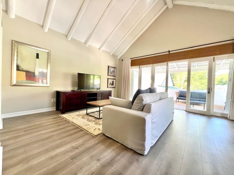 Bright living room featuring vaulted ceilings with exposed beams, modern laminate flooring, and large sliding glass doors providing access to the outdoor patio area.