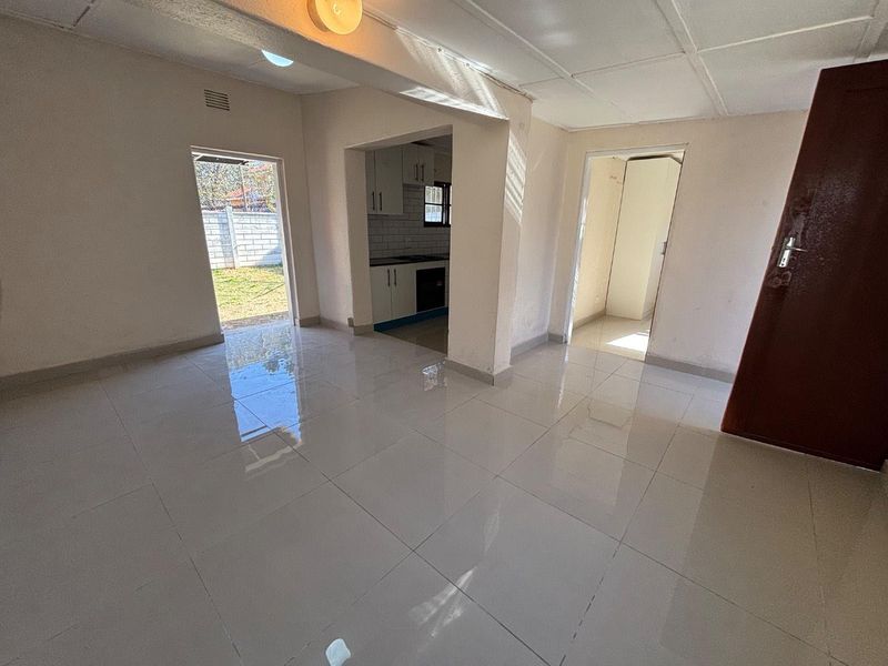 An open-plan living area featuring white tiled flooring, leading into a compact kitchen with built-in cabinetry and an integrated oven.