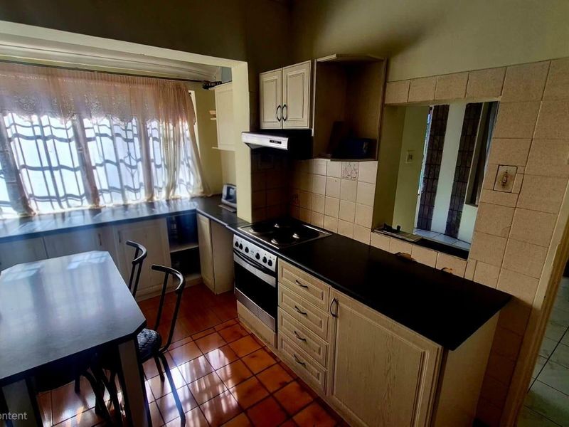 A dated kitchen featuring built-in cabinetry, a built-in oven with hob, extractor fan, and tiled flooring, offering potential for a modern renovation.