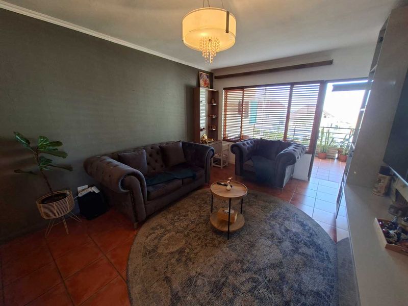 A living room featuring terracotta floor tiles, a large window with blinds, and direct access to an outdoor balcony area.