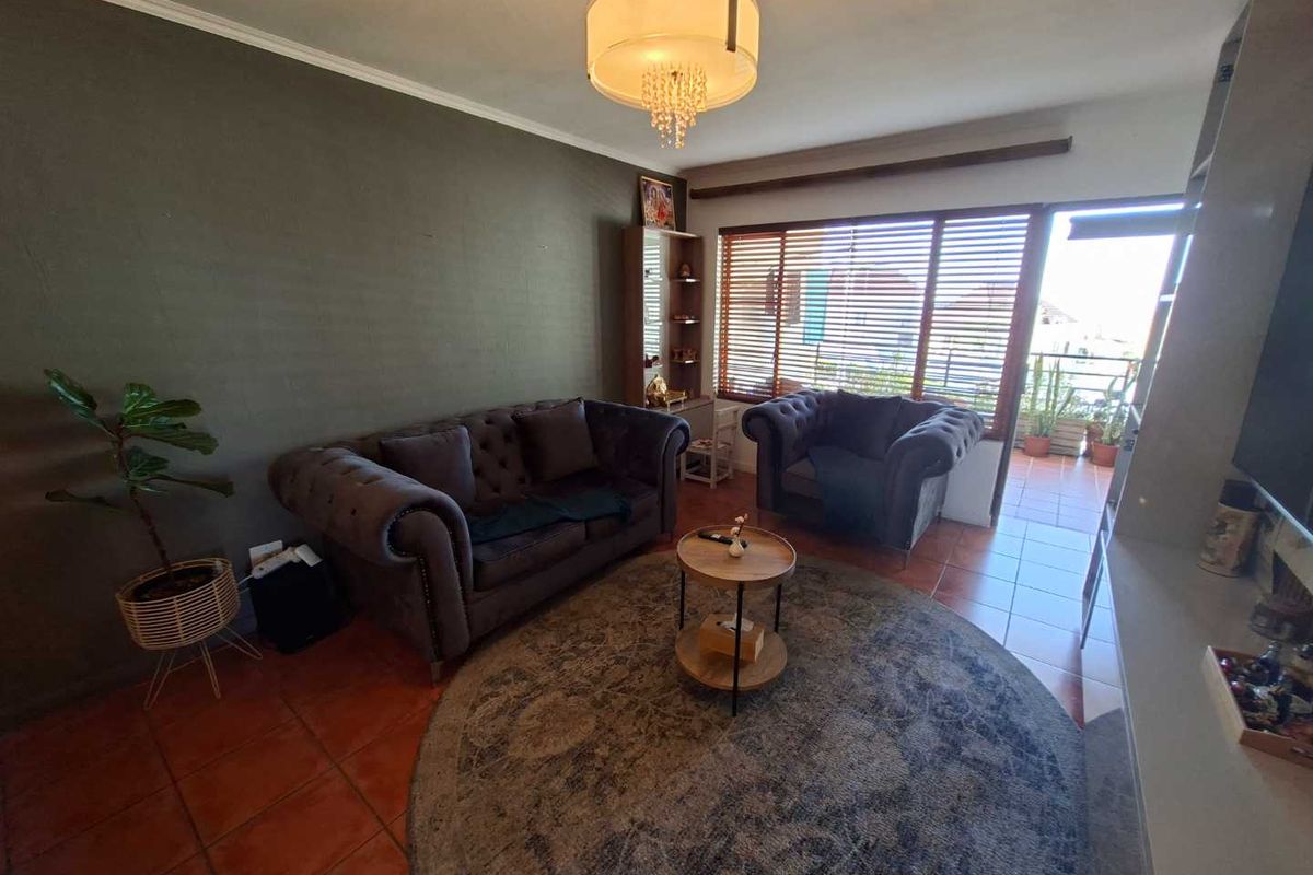 A living room featuring terracotta floor tiles, a large window with blinds, and direct access to an outdoor balcony area.
