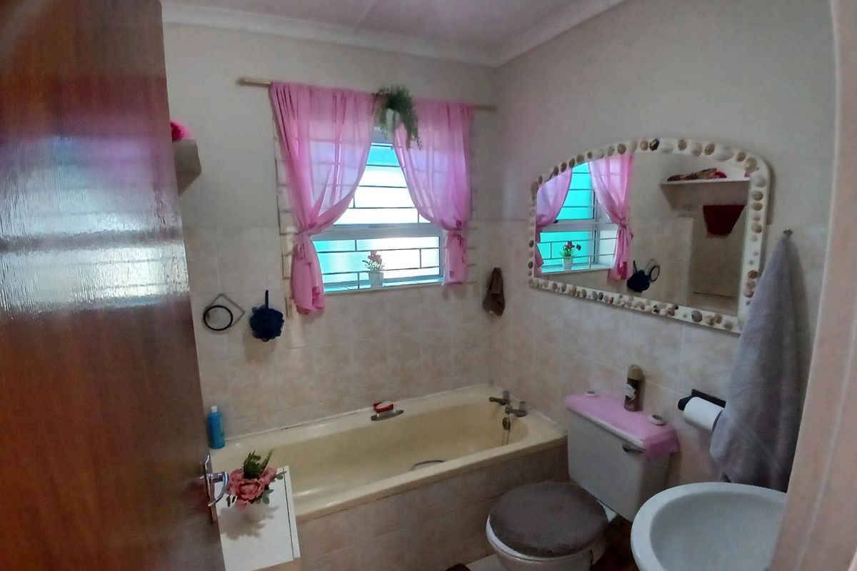 A functional bathroom featuring a built-in bathtub, standard toilet, and wall-mounted basin with tiled splashbacks and a window for natural light.