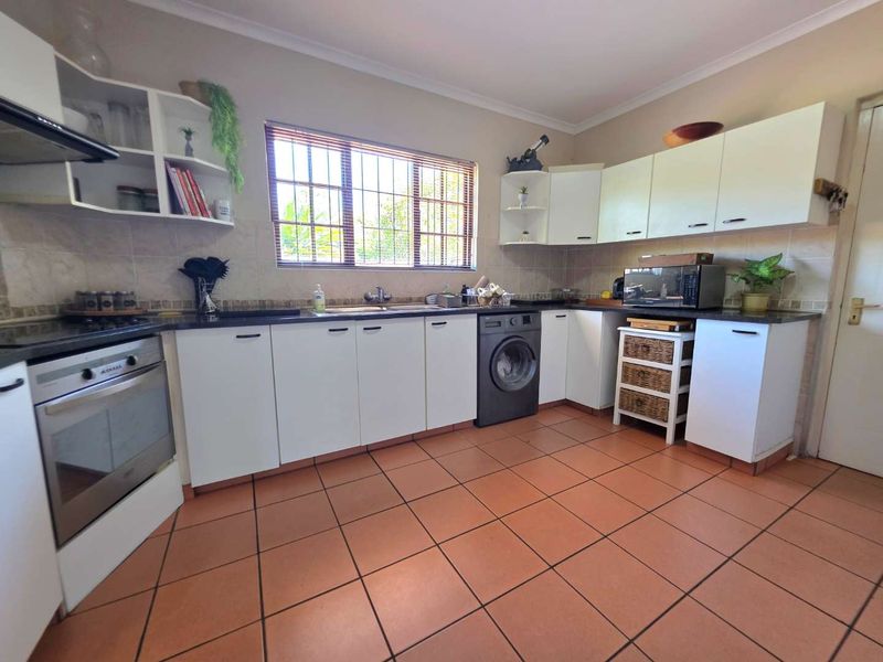A functional kitchen featuring white cabinetry, tiled flooring, a built-in oven with extractor fan, and a tiled backsplash with a window overlooking the exterior.