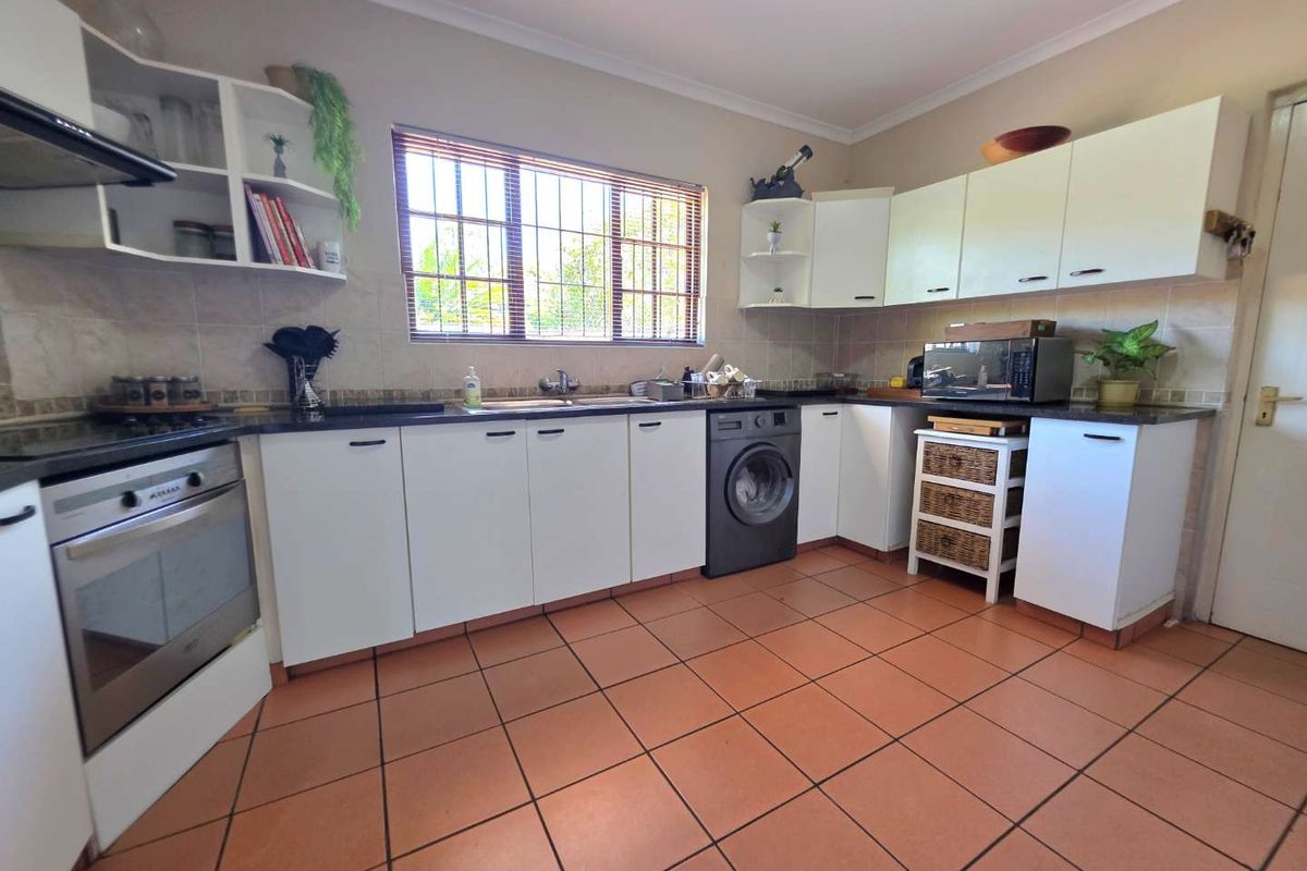 A functional kitchen featuring white cabinetry, tiled flooring, a built-in oven with extractor fan, and a tiled backsplash with a window overlooking the exterior.