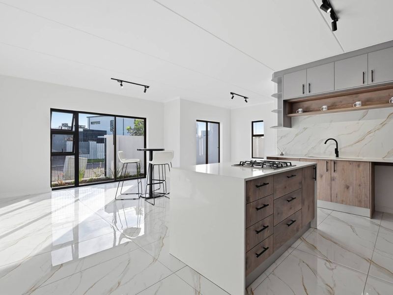 Modern open-plan kitchen and living area featuring a central island with gas cooktop, marble-look tiling, and contemporary cabinetry with high-end finishes.