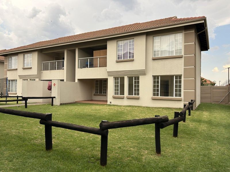 Rear view of a two-story townhouse featuring a stucco facade, terracotta roof tiles, a private balcony, and a shared garden area with timber fencing.