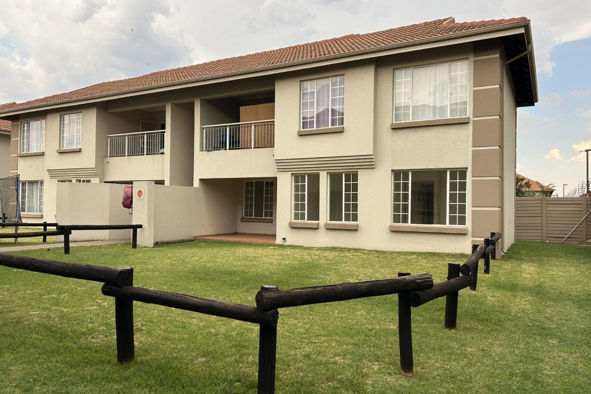 Rear view of a two-story townhouse featuring a stucco facade, terracotta roof tiles, a private balcony, and a shared garden area with timber fencing.