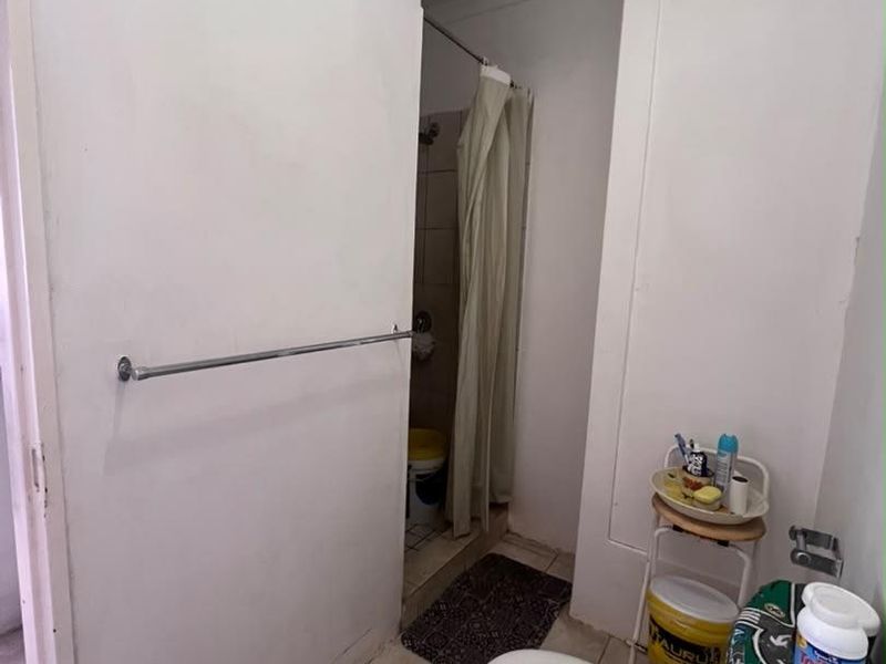 A functional bathroom featuring a shower, toilet, and washbasin with tiled flooring and an extractor fan.