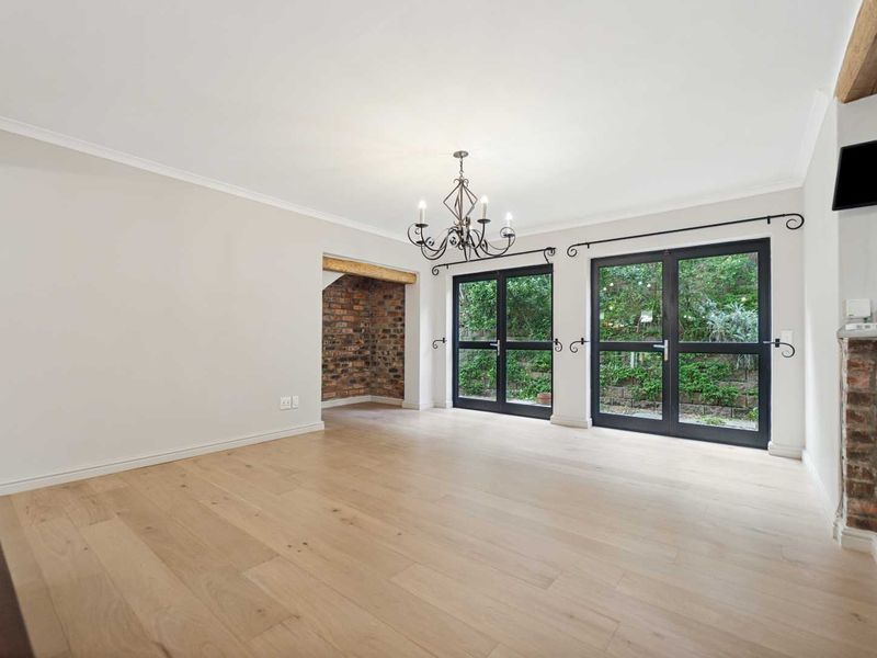 Spacious living area featuring light timber flooring, exposed brick accents, a decorative chandelier, and double french doors opening to the rear garden.