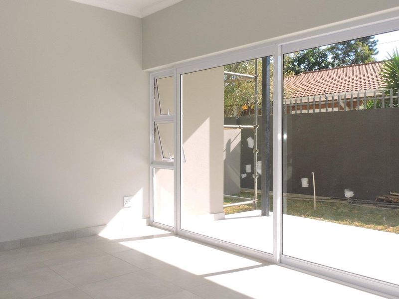 A bright, empty living room featuring large sliding glass doors that provide access to an outdoor area with tiled flooring.