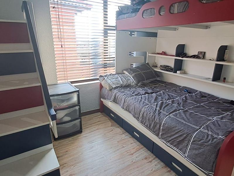 A compact bedroom featuring laminate flooring and venetian blinds, providing a functional space with natural light.