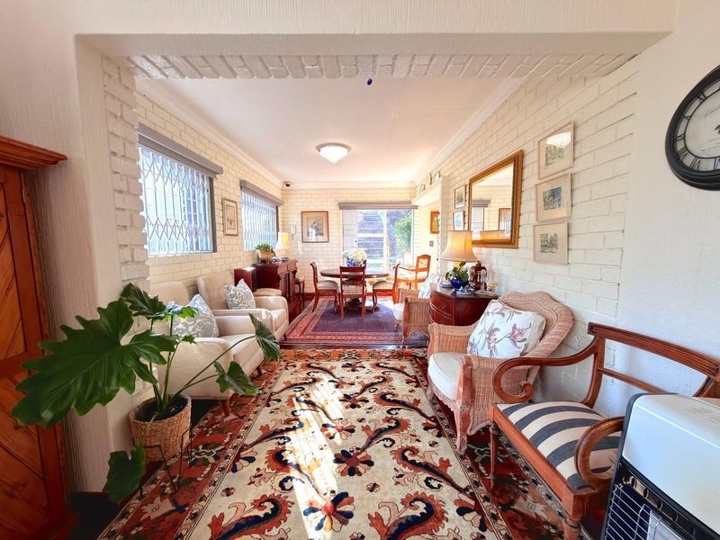 A cozy living room featuring exposed white-painted brick walls, security bars on windows, and a bright, open layout leading to a dining area.