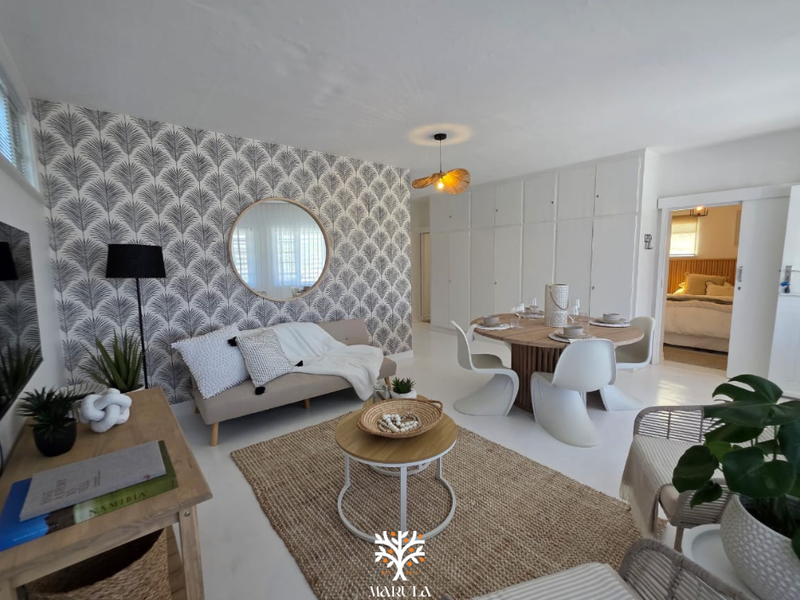 Bright open-plan living and dining area featuring built-in floor-to-ceiling storage cupboards and a sliding door leading to the bedroom.