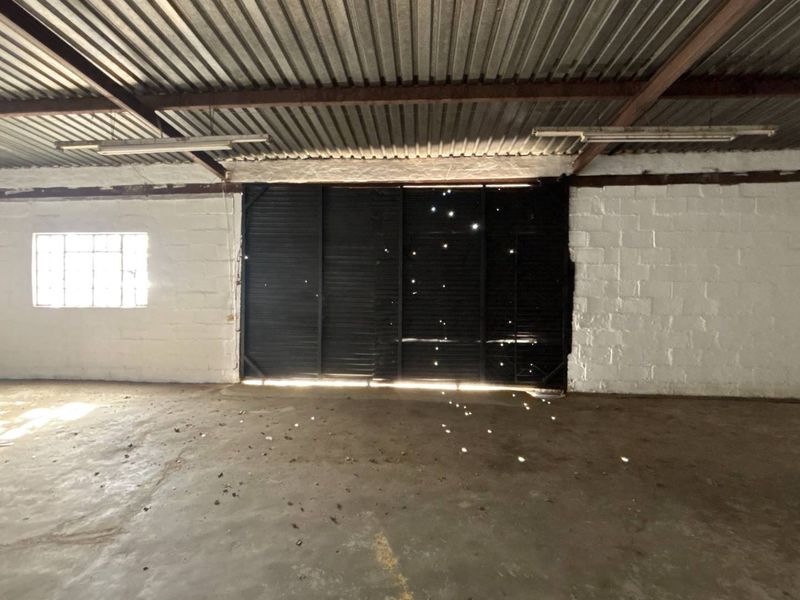 Spacious industrial utility area featuring exposed steel trusses, corrugated metal roofing, concrete flooring, and a large sliding access door.