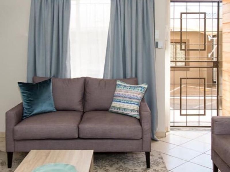 A living room area featuring tiled flooring, a window with curtains, and a security gate leading to the exterior.