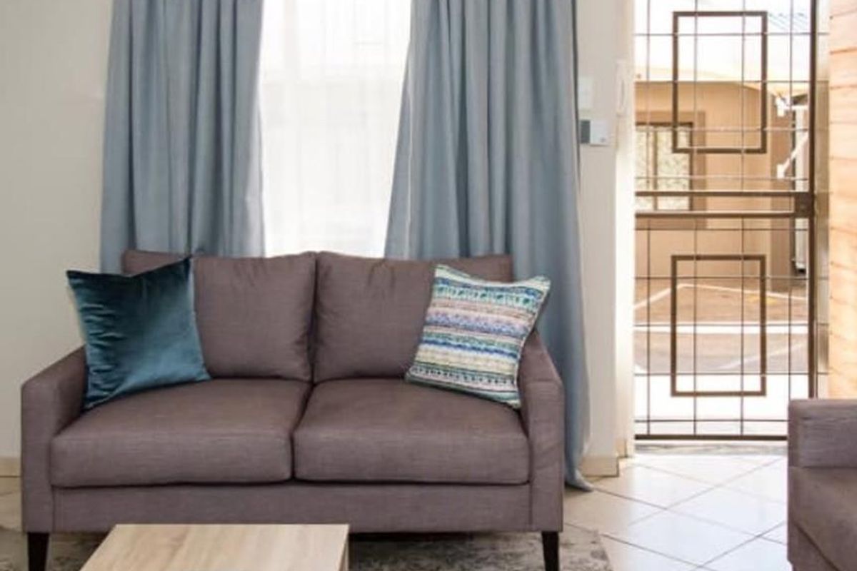 A living room area featuring tiled flooring, a window with curtains, and a security gate leading to the exterior.