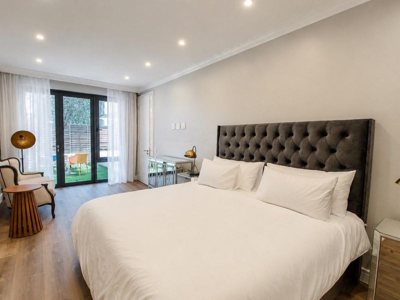A well-maintained bedroom featuring modern laminate flooring, recessed downlighting, and direct access to an outdoor patio area through sliding glass doors.