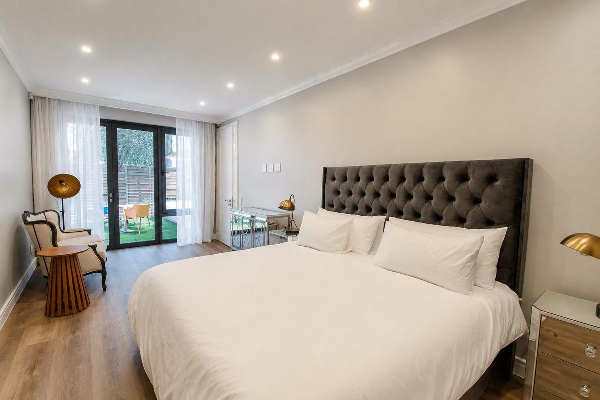 A well-maintained bedroom featuring modern laminate flooring, recessed downlighting, and direct access to an outdoor patio area through sliding glass doors.