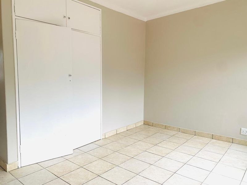 An empty bedroom featuring neutral wall paint, ceramic floor tiles, and built-in storage cupboards.