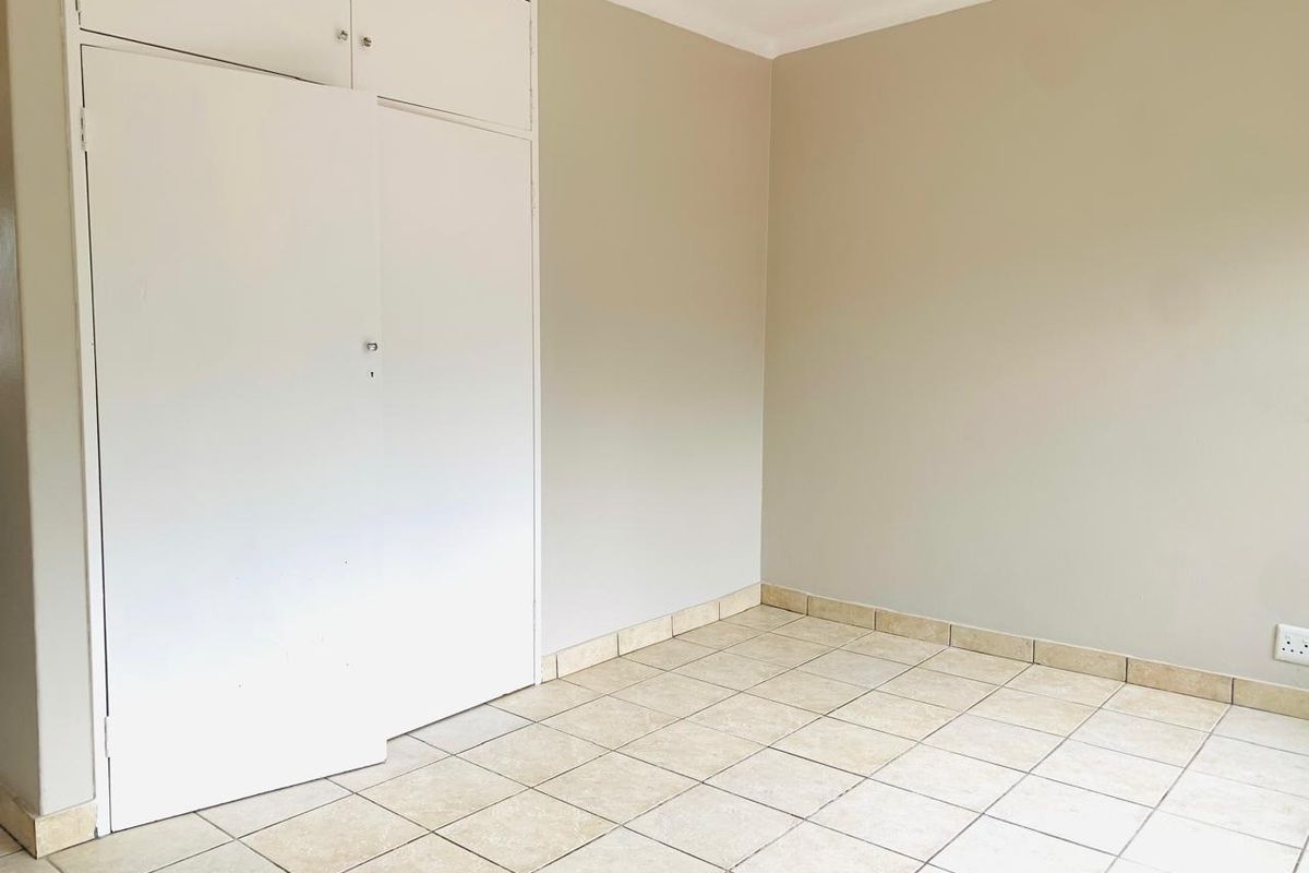 An empty bedroom featuring neutral wall paint, ceramic floor tiles, and built-in storage cupboards.