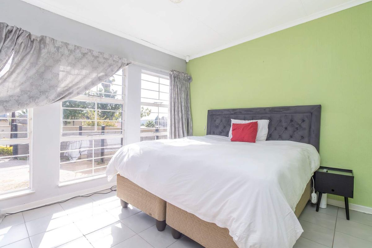 A bedroom featuring tiled flooring and large windows with security bars, finished with a bright green accent wall.
