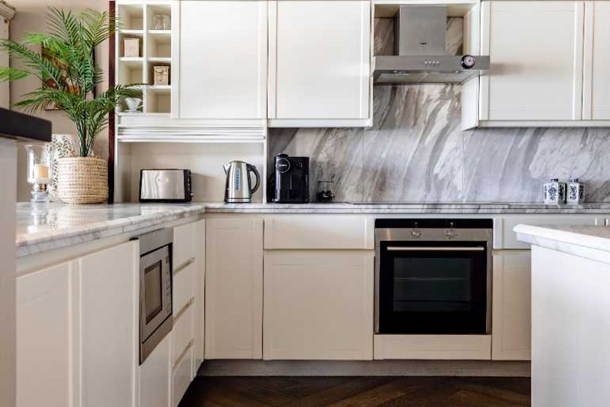 Modern kitchen featuring white cabinetry, marble countertops and backsplash, built-in appliances, and elegant dark herringbone hardwood flooring.