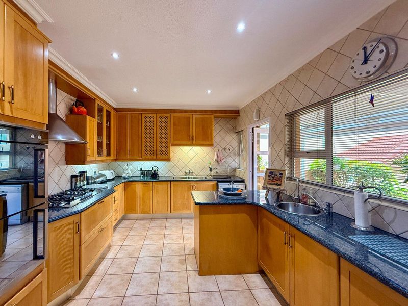 A functional kitchen featuring warm-toned wooden cabinetry, granite countertops, a gas hob, built-in oven, and tiled flooring with ample natural light.