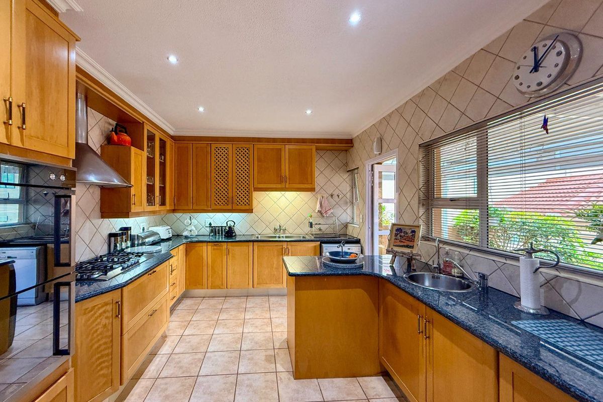 A functional kitchen featuring warm-toned wooden cabinetry, granite countertops, a gas hob, built-in oven, and tiled flooring with ample natural light.