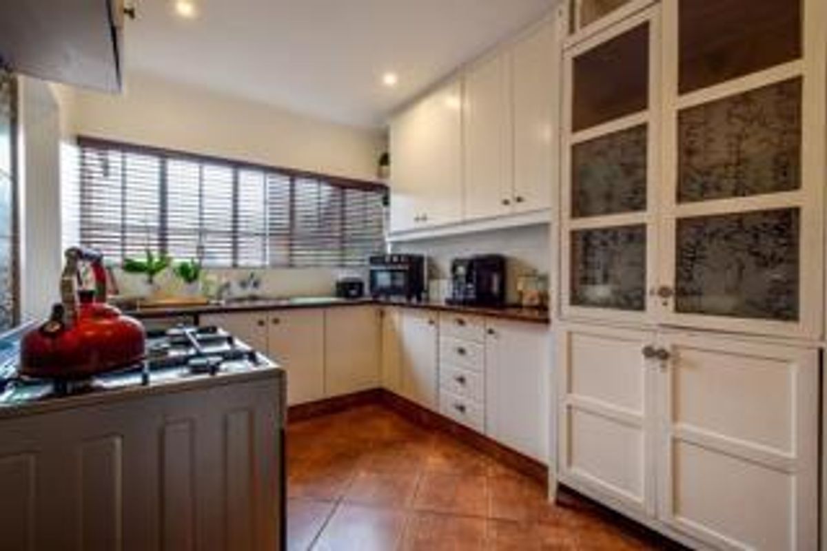 A functional kitchen featuring white cabinetry, a gas hob, and a tall pantry cupboard with glass-paneled doors, set against tiled flooring.