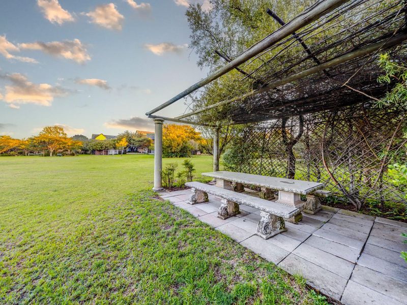 A well-maintained garden area featuring a stone pergola with an integrated stone table and bench set on a paved patio.