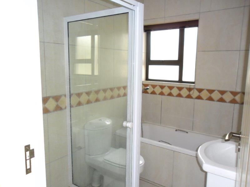 A functional bathroom featuring a shower enclosure, bathtub, pedestal sink, and toilet with neutral wall tiling.