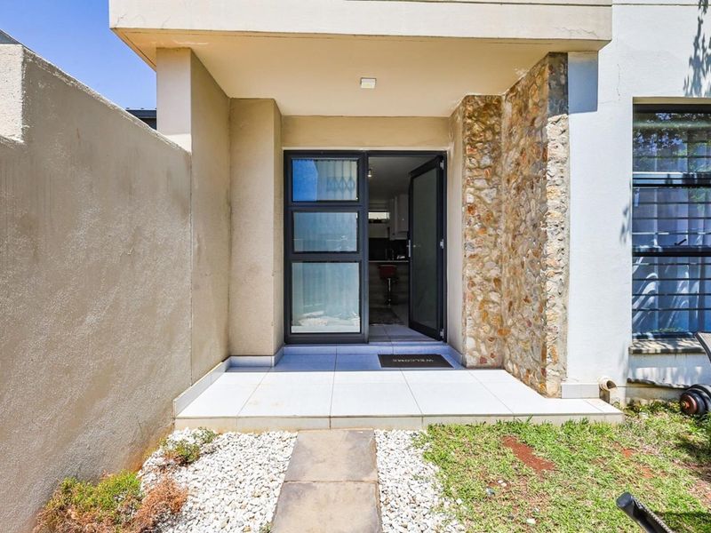 A modern townhouse entrance featuring a tiled porch, stone cladding detail, and a secure aluminium-framed glass door.