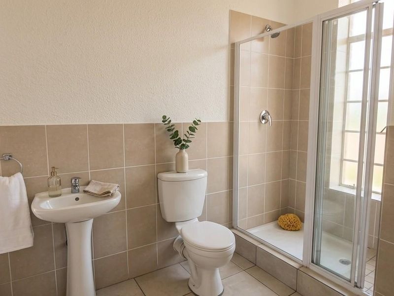 A functional bathroom featuring a pedestal basin, toilet, and a glass-enclosed shower with neutral wall and floor tiling.