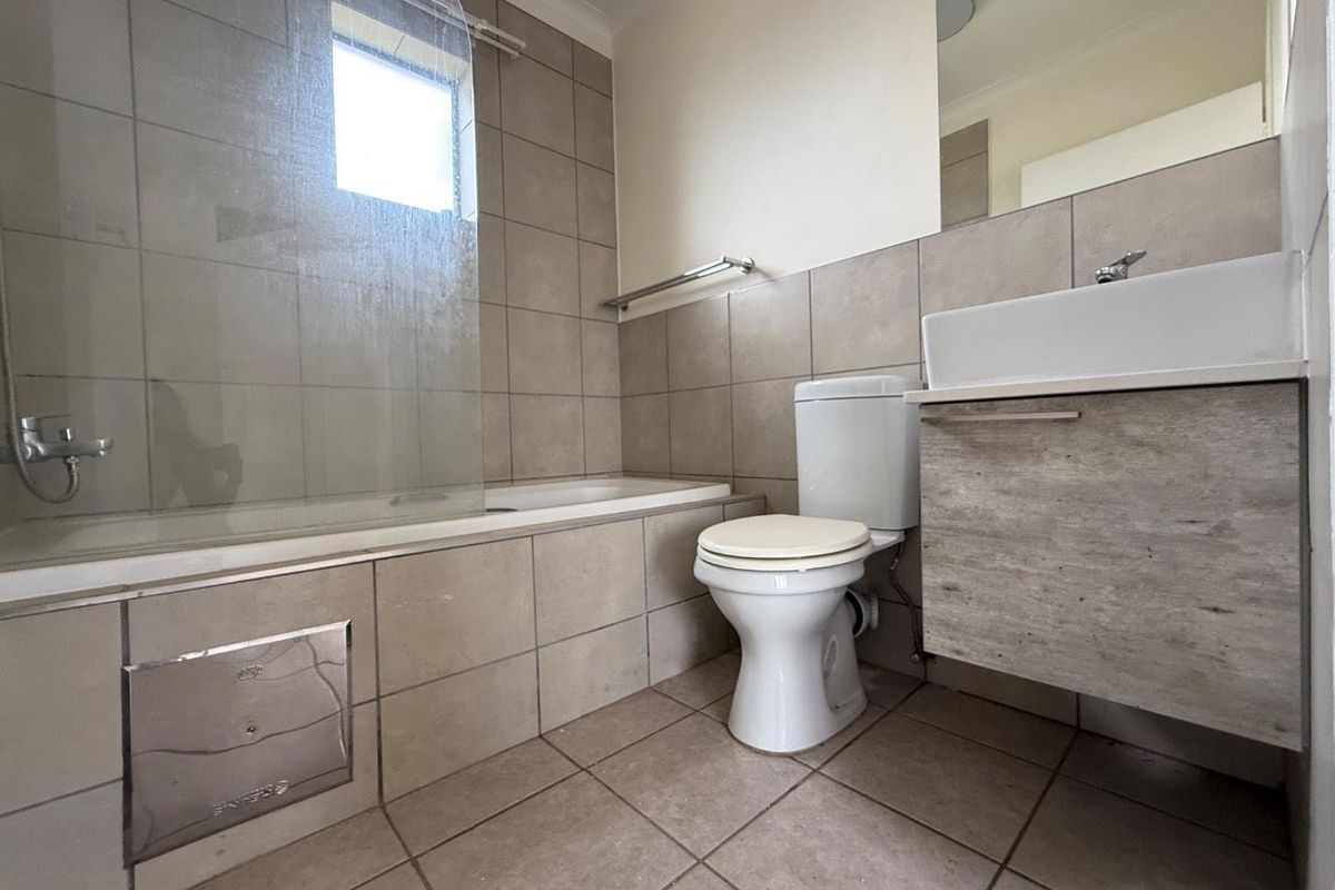 A functional bathroom featuring a tiled bathtub with glass screen, wall-mounted vanity, and standard toilet suite with neutral ceramic tiling.