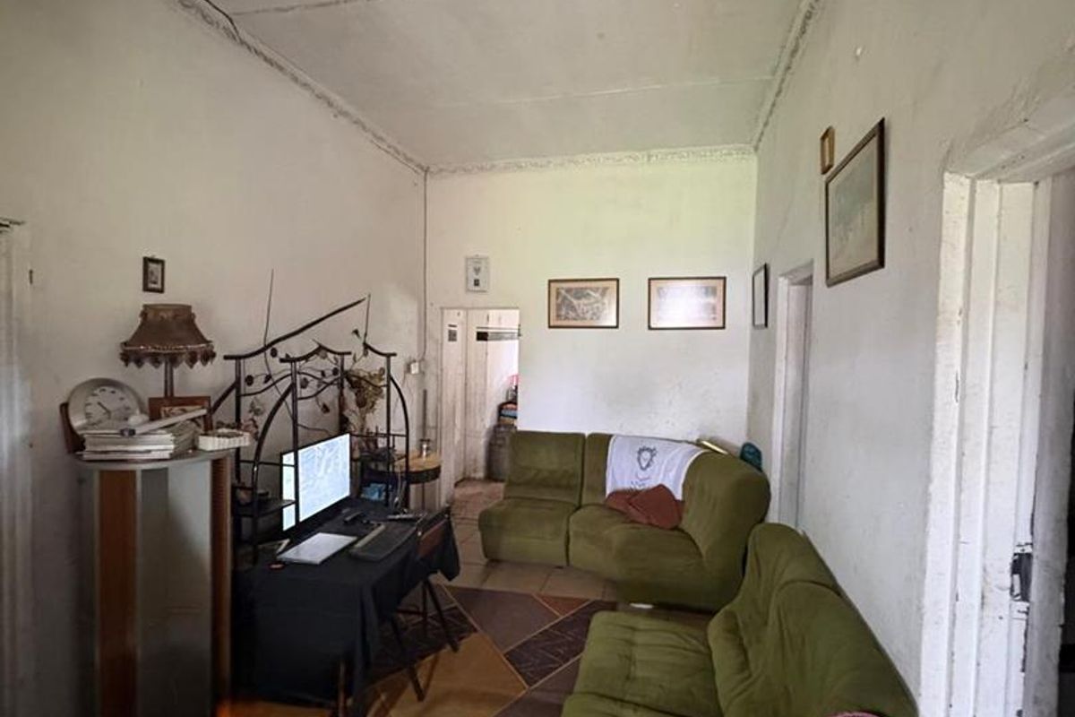 A living room area featuring tiled flooring and a high ceiling with visible signs of wear and aging.