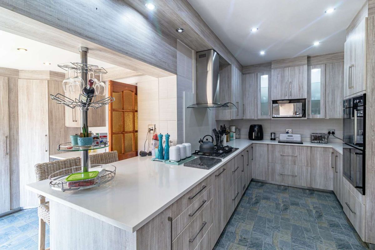 Modern kitchen featuring light wood-grain cabinetry, stone countertops, a built-in oven, extractor fan, and gas hob, complemented by slate-style floor tiling.