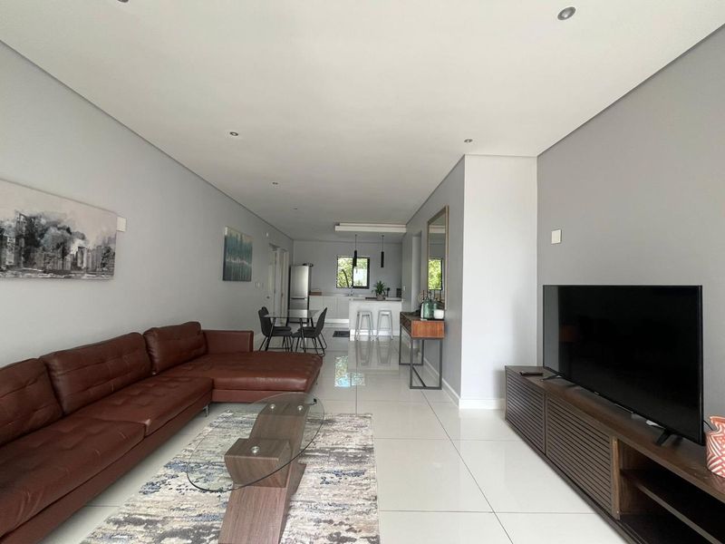 Spacious open-plan living and kitchen area featuring modern porcelain floor tiles, recessed lighting, and a functional kitchen island with pendant lights.