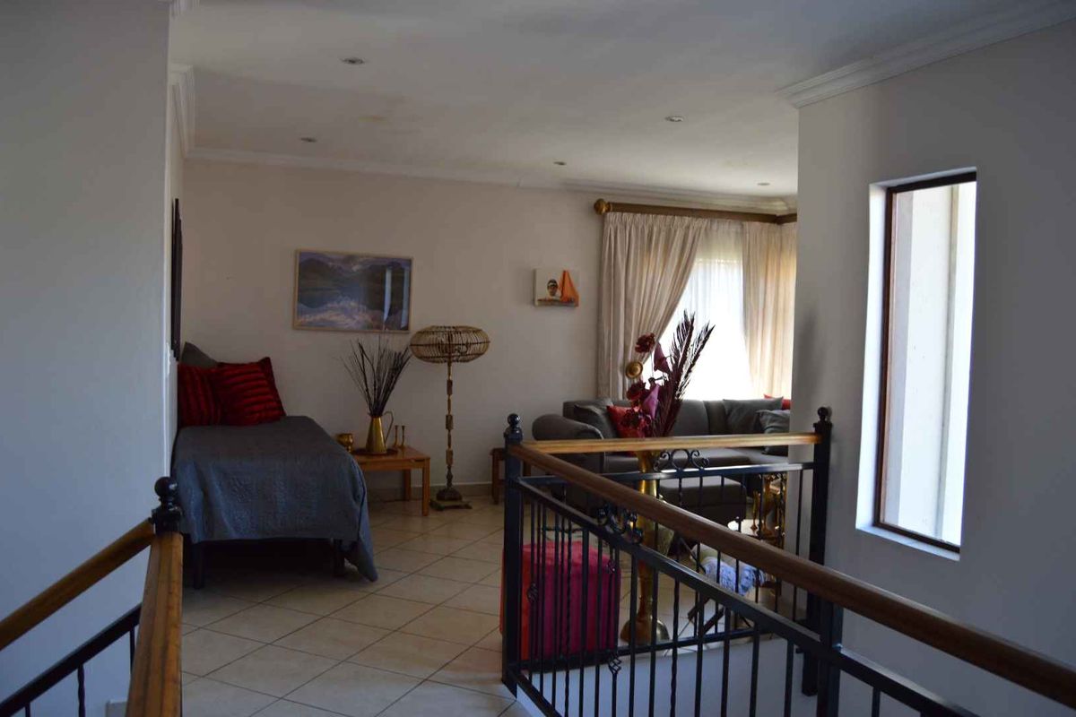 An open-plan living area featuring tiled flooring, recessed lighting, and a decorative wrought iron balustrade overlooking the lower level.