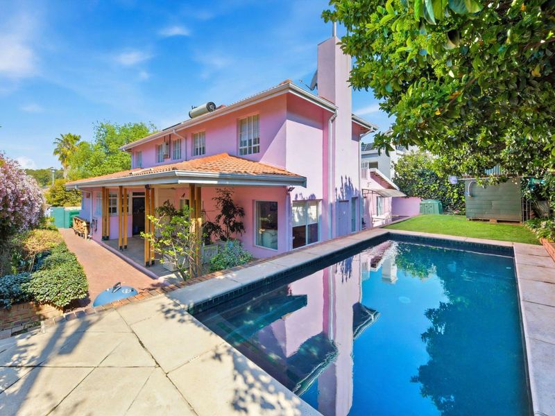 Rear exterior view of the house featuring a swimming pool, paved pool deck, and a covered patio area with a pink facade.